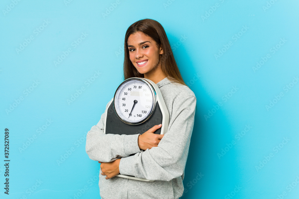 Young caucasian woman holding a scale isolated on a blue background Young caucasian woman holding a scale isolated on a blue background