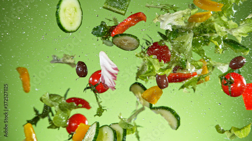 Fototapeta Naklejka Na Ścianę i Meble -  Flying vegetable salad isolated on green background. Healthy eating and lifestyle.