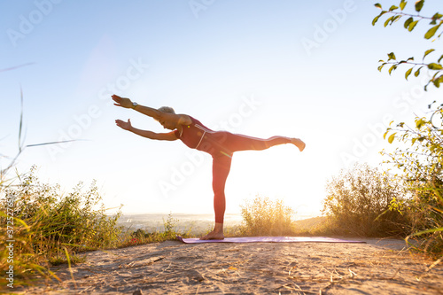 Girl doing yoga exercise two hands up on a sports mat at sunrise and trying to do a Balancing Stick