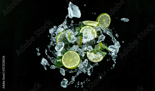 Fresh ripe limes with ice cubes flying on a black background. Freeze motion.