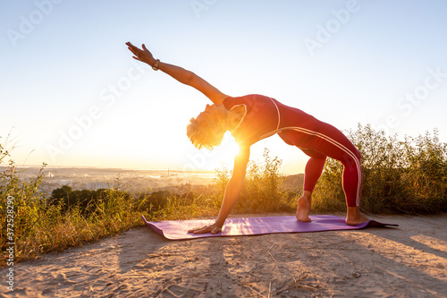 Woman doing Wheel half Moon power Pose lift up one hand in the sunrise