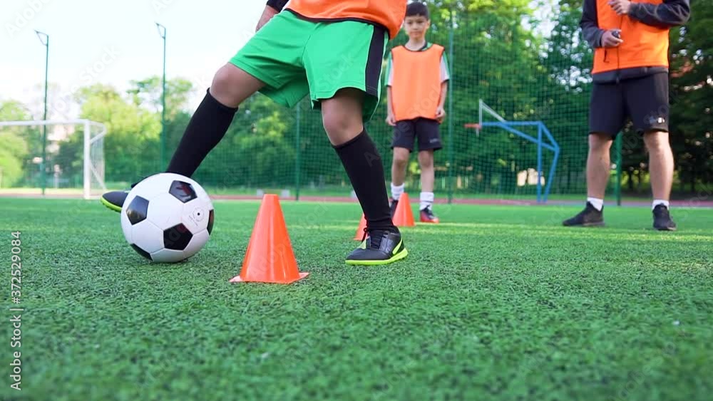 Football concept where brisk teen boy in football uniform training with ball around small racks to improve his speed during workout on the soccer field Football concept where brisk teen boy in football uniform training with ball around small racks to improve his speed during workout on the soccer field