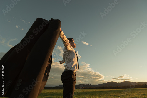 Businessman celebrating success, standing in beautiful meadow with his arms spread widely