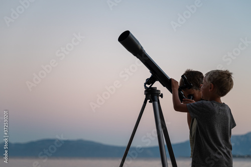 Two brothers looking at the stars using a telescope by the sea photo