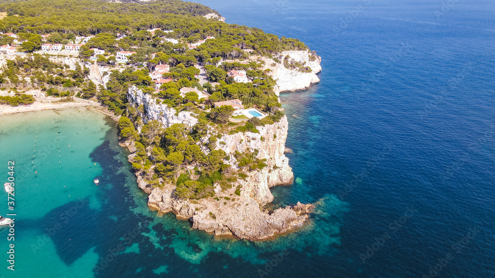 Beautiful aerial view of mediterranean bay with cliffs and holiday houses with swimming pools in Menorca, Spain Cala Galdana, aerial top view drone photo