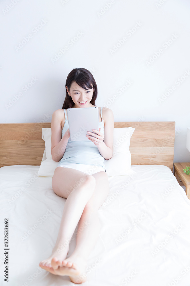 ベッドでタブレットPCを見る女性