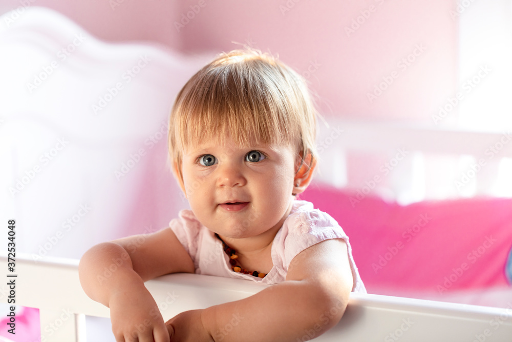 blond baby with blue eyes looking at camera. baby standing in the crib. blond baby with blue eyes looking at camera. baby standing in the crib.