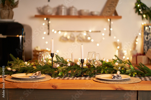 The festive Christmas table is decorated with branches of a Christmas tree, candles and garlands. Cozy home Christmas atmosphere. photo