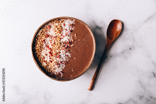 Chocolate Smoothie from Banana and Strawberries with cacao, Granola and Coconut Shreds on top in Coconut Shell Bowl, strong shadows. Healthy summer breakfast, top view