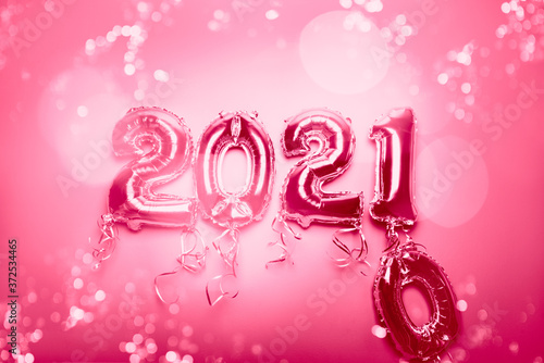 Cnanging of Year 2020 to New Year 2021 made from Silver Number Balloons. Holiday Party Decoration or postcard concept with xmas lights, on pink background