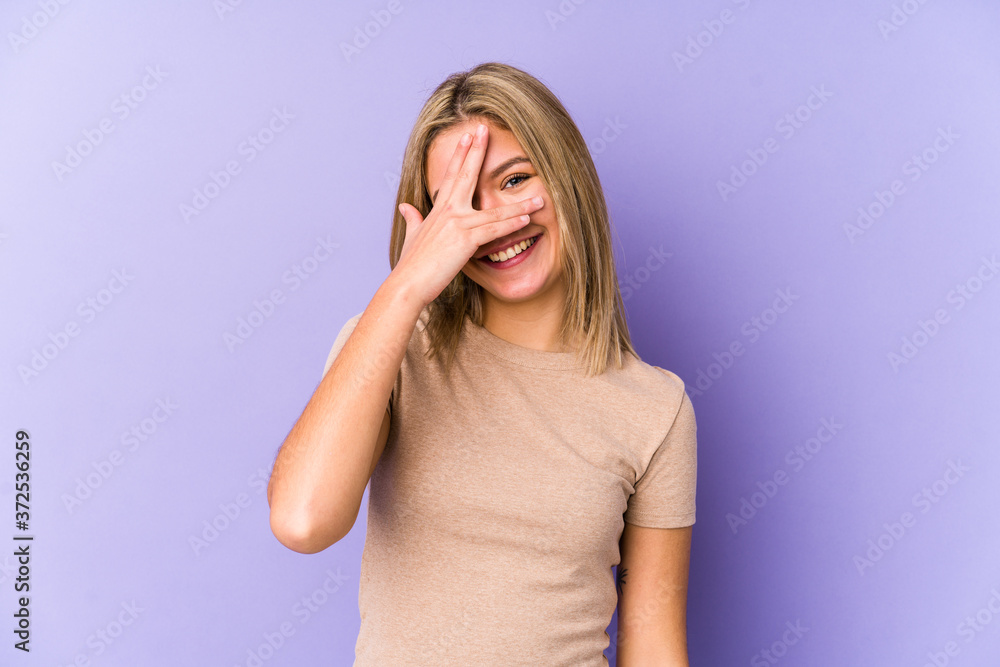 Young blonde caucasian woman isolated blink at the camera through fingers, embarrassed covering face. Young blonde caucasian woman isolated blink at the camera through fingers, embarrassed covering face.