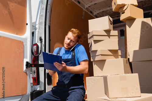Loader in uniform holding clipboard while talking on smartphone near packages in truck © LIGHTFIELD STUDIOS