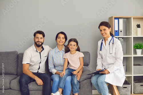 Portrait of a doctor and a happy family are looking at the camera in the clinic office.