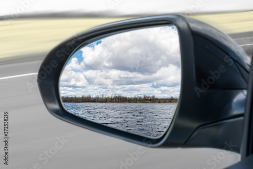 in the mirror of the car you can see a forest lake and large clouds in autumn or spring