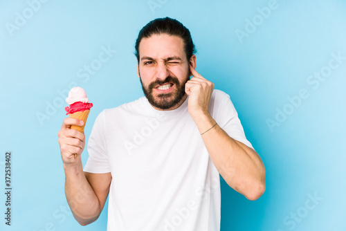 Young caucasian man eating an ice cream isolated covering ears with hands.