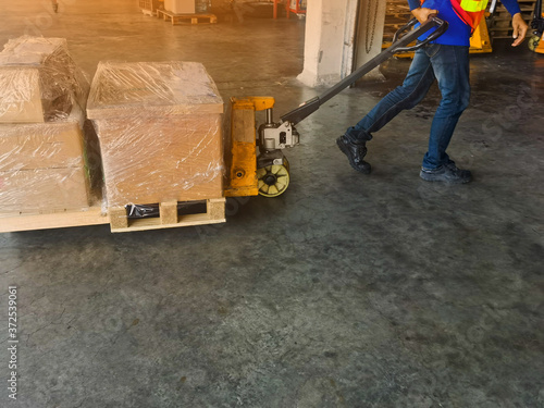 Worker driving forklift loading shipment carton boxes and goods on wooden pallet at loading dock from container truck to warehouse cargo storage in freight logistics and transportation industrial