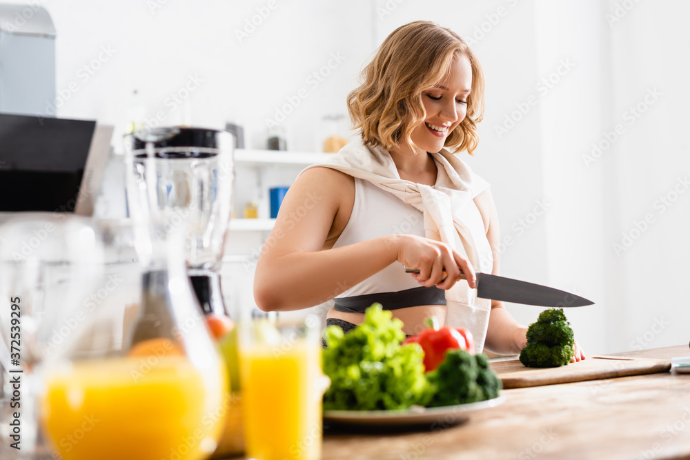 selective focus of woman cutting fresh broccoli on chopping board near jug with orange juice