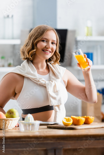 woman holding glass with fresh orange juice and looking at camera