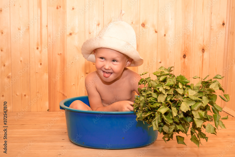 A child with a broom is sitting in a tub at the site. Traditional Russian bath. Funny hat, wellness treatments, little boy with bath hat and broom A child with a broom is sitting in a tub at the site. Traditional Russian bath. Funny hat, wellness treatments, little boy with bath hat and broom