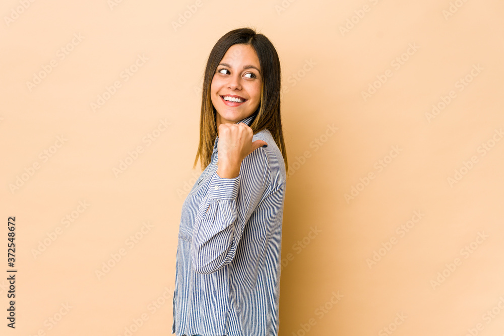 Young woman isolated on beige background points with thumb finger away, laughing and carefree. Young woman isolated on beige background points with thumb finger away, laughing and carefree.