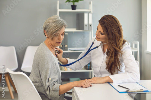 Female doctor listens with stethoscope to patient. Senior man sitting in clinic office.
