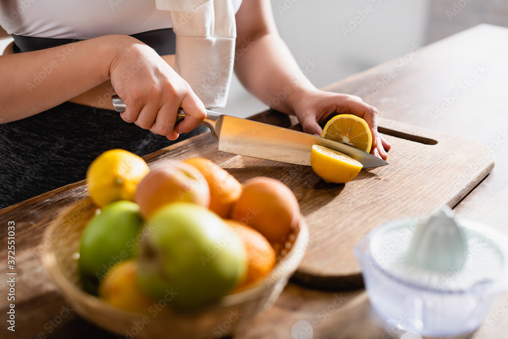 cropped view of young woman cutting fresh lemon on chopping board near fruits and juicer cropped view of young woman cutting fresh lemon on chopping board near fruits and juicer