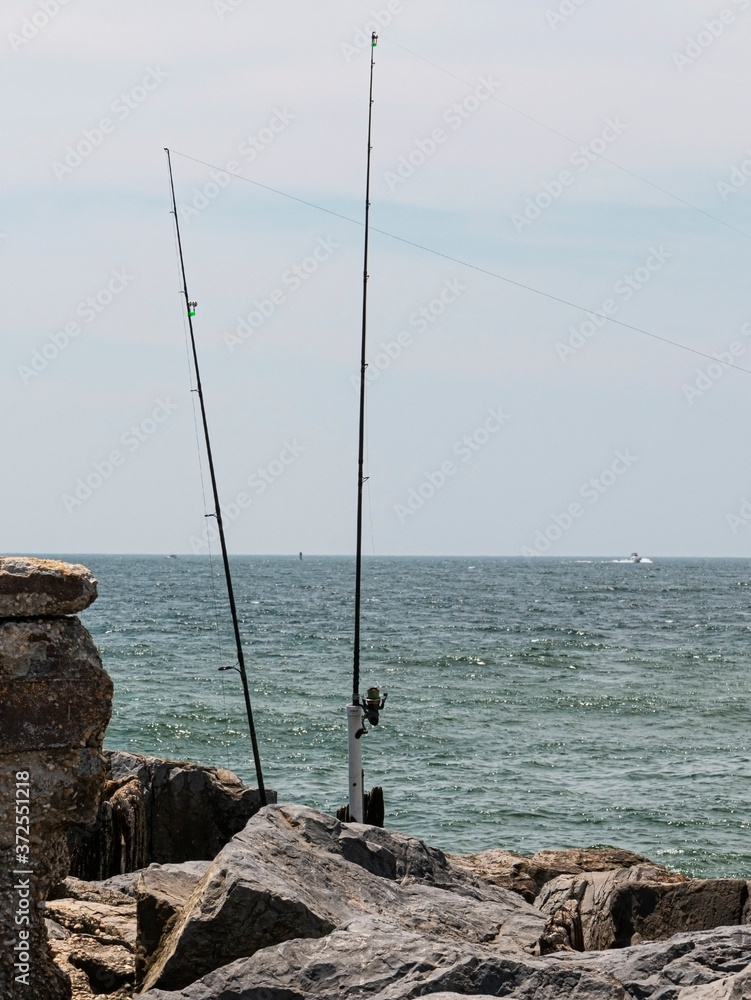 Two fishing poles standing on a rock jetty fishing at the ocean