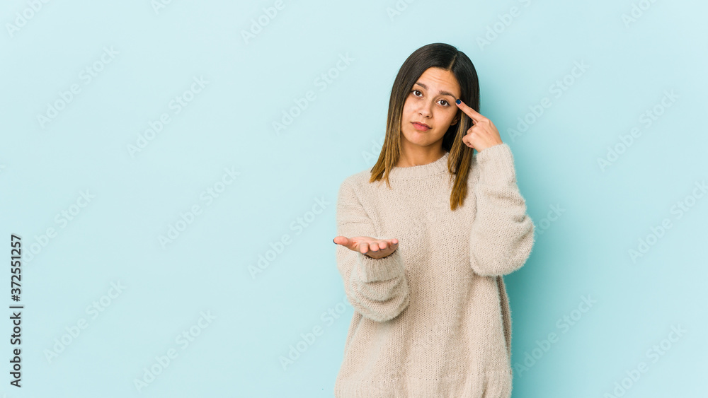 Young woman isolated on blue background holding and showing a product on hand. Young woman isolated on blue background holding and showing a product on hand.