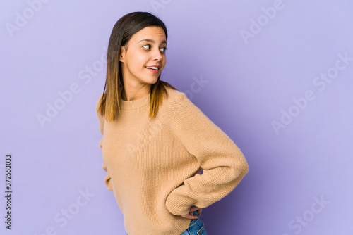 Young woman isolated on purple background looks aside smiling, cheerful and pleasant.