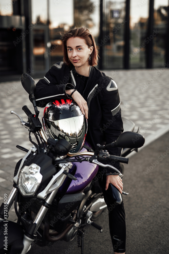 Smiling girl in a motorcycle jacket sits with a motorcycle helmet on a motorbike Smiling girl in a motorcycle jacket sits with a motorcycle helmet on a motorbike