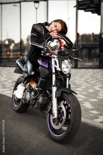 Pretty lady in a black jacket sits on a purple motorbike with a red safety helmet