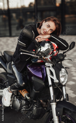 Super pretty girl in a black jacket sits on a purple motorbike with a red safety helmet