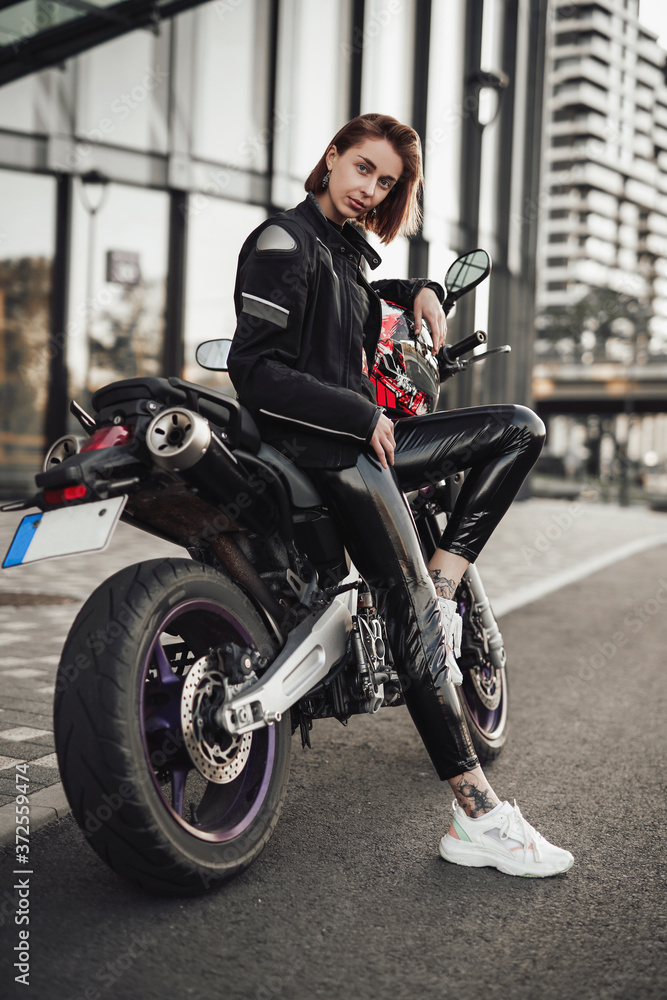 Hot looking girl in a black jacket sits on a purple motorbike with a red safety helmet