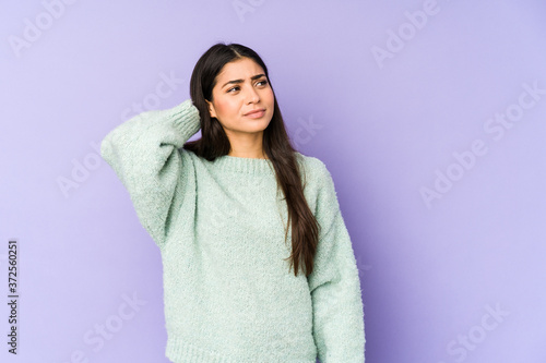 Young indian woman isolated on purple background touching back of head, thinking and making a choice. © Asier