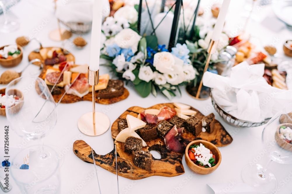 A cutting board with delicacies on the table with a white tablecloth and candles in candlesticks.