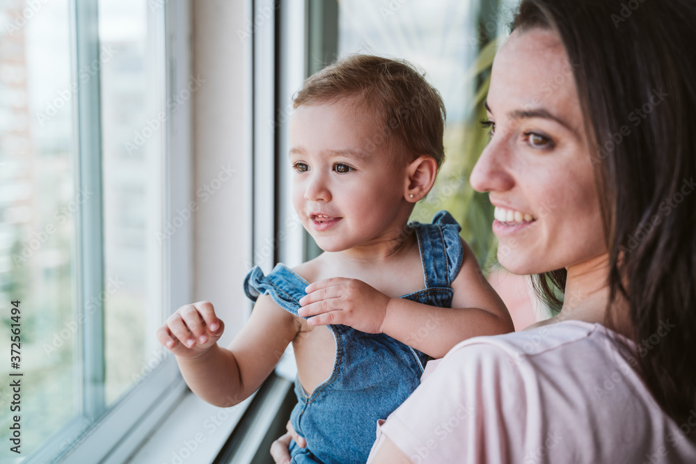 Mother with baby girl at home looking by the window Mother with baby girl at home looking by the window