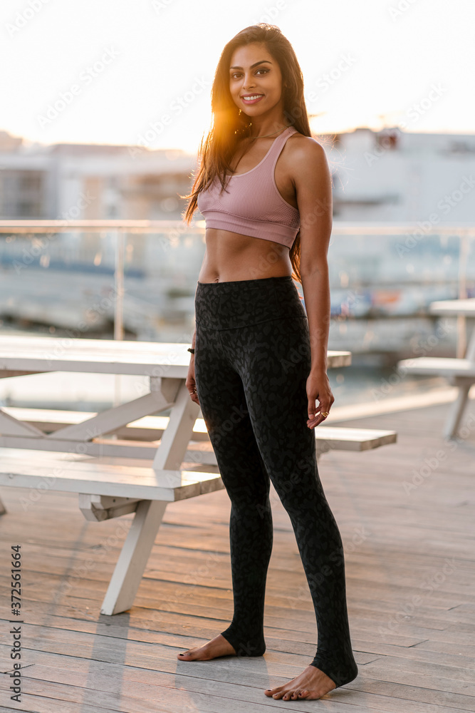 Smiling female athlete standing on pier against clear sky during sunset Smiling female athlete standing on pier against clear sky during sunset