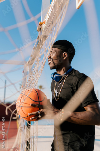 Young man holding basketball looking away while standing by net in court photo