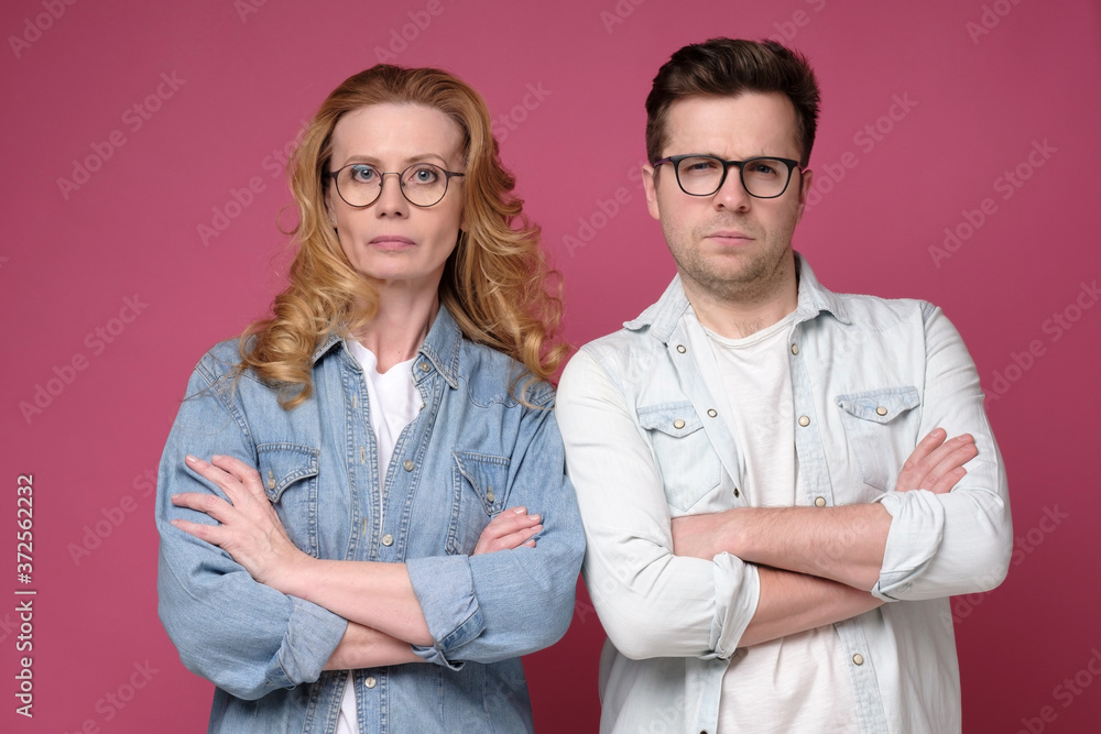 Serious business team of mature man and woman in glasses looking at camera. Studio shot on pink wall. Serious business team of mature man and woman in glasses looking at camera. Studio shot on pink wall.