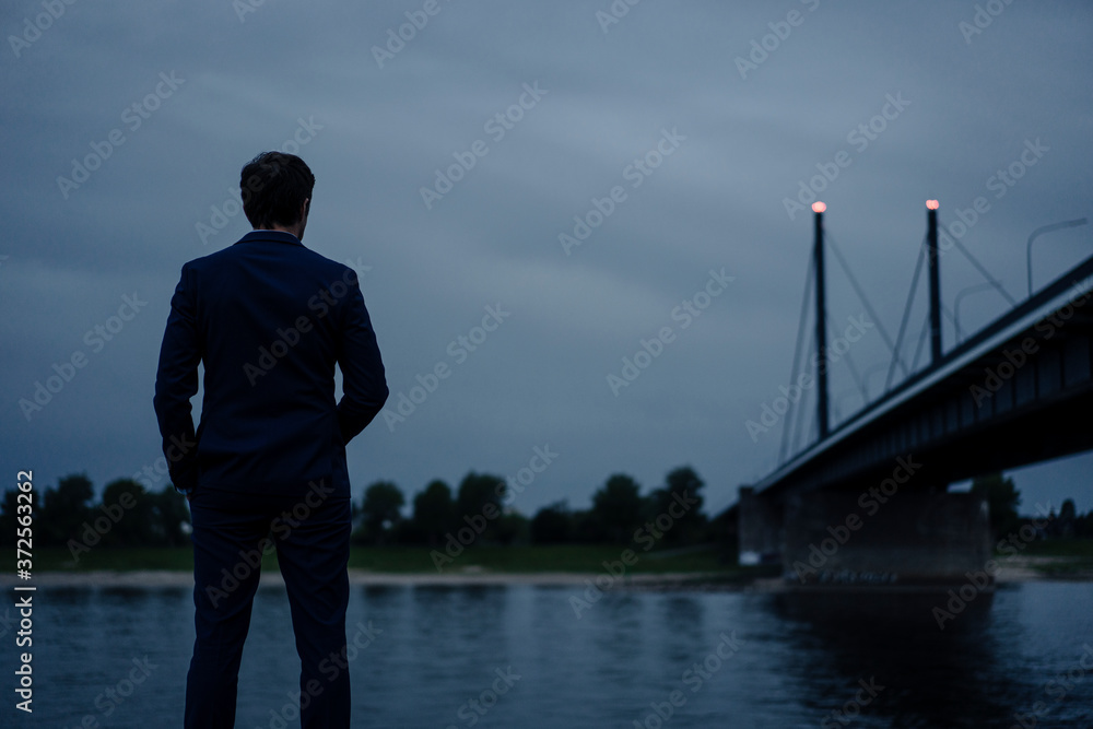 Mature businessman standing at the riverbank at dusk Mature businessman standing at the riverbank at dusk