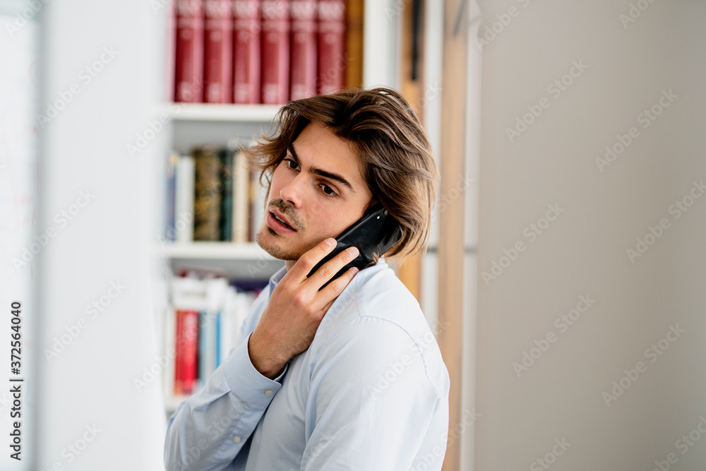 Male professional talking over smart phone looking away while sitting in office Male professional talking over smart phone looking away while sitting in office