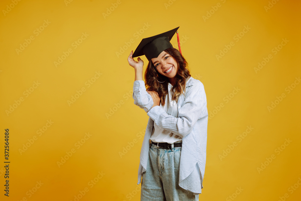 Graduate woman in a graduation hat on her head posing on a yellow background. Study, education, university, college, graduate concept. Graduate woman in a graduation hat on her head posing on a yellow background. Study, education, university, college, graduate concept.
