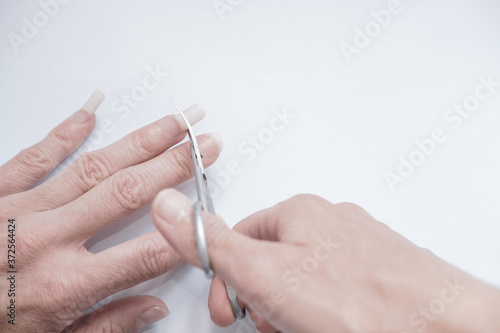 Two hand closeup  hand with nail scissors cuts long nails on a woman s hand in the process of cutting nails. Manicure and fingernail trimming.