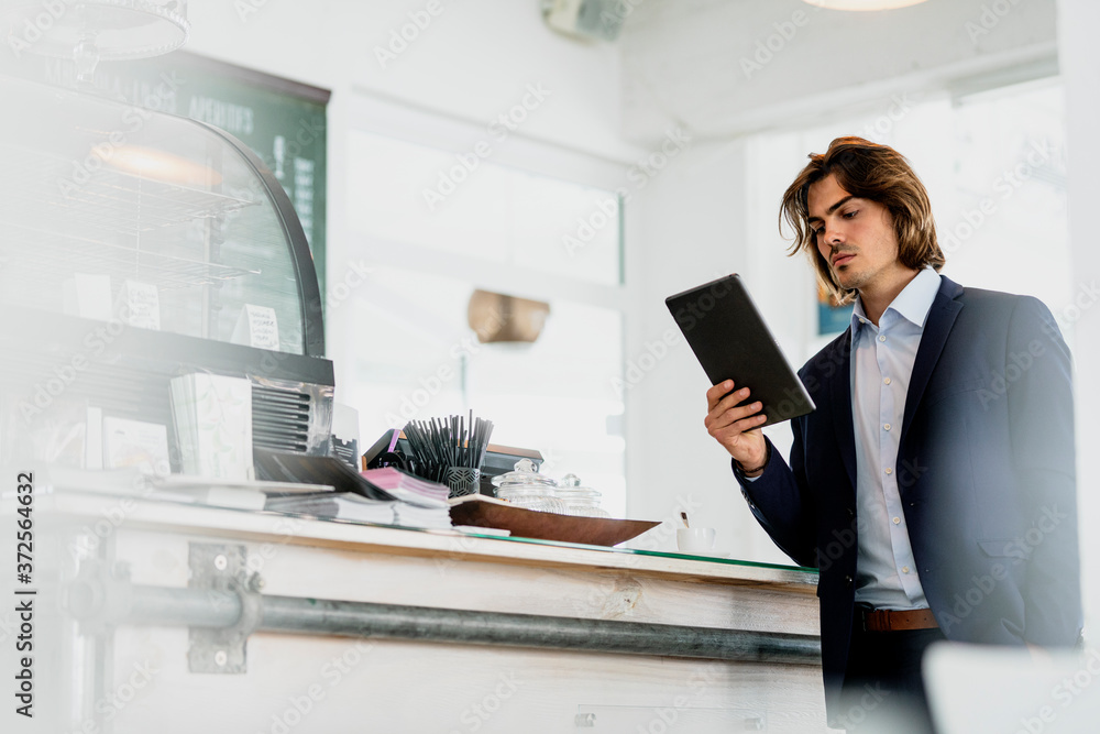 Male entrepreneur using digital tablet while standing in coffee shop Male entrepreneur using digital tablet while standing in coffee shop