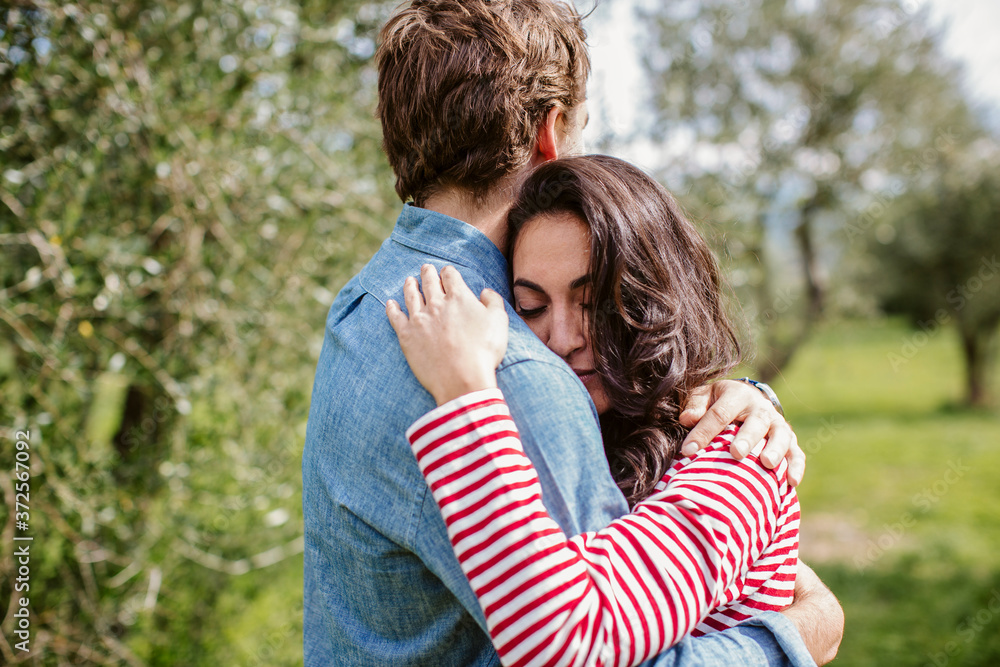 Romantic young couple embracing while standing against trees Romantic young couple embracing while standing against trees