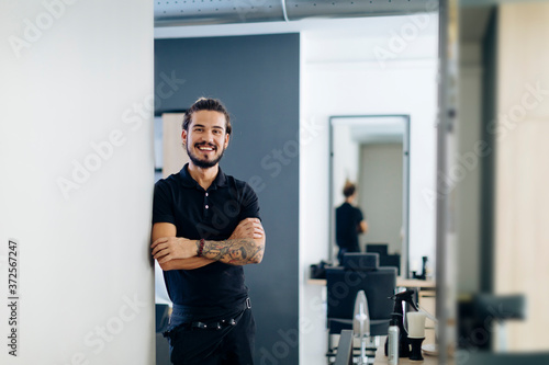 Confident male barber standing arms crossed in hair salon