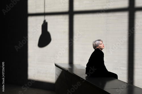 Female professional wearing black suit relaxing on retaining wall with sunlight and shadow in background at office photo