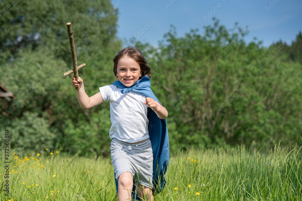Playful boy wearing cape holding toy sword while running on grassy land Playful boy wearing cape holding toy sword while running on grassy land