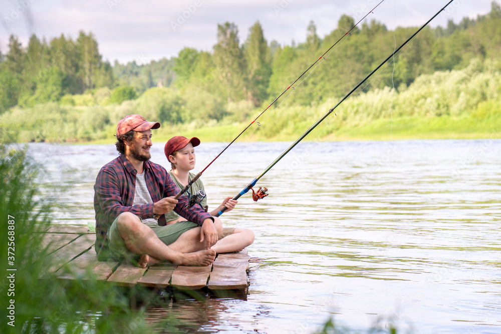 Father and son fishing while sitting on boardwalk at riverbank Father and son fishing while sitting on boardwalk at riverbank