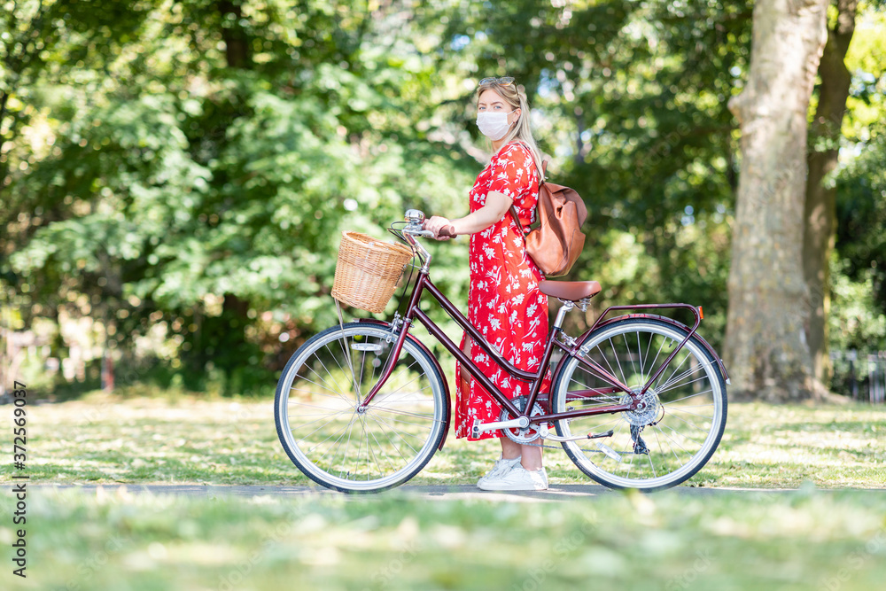 Woman wearing mask while standing with bicycle on footpath in park Woman wearing mask while standing with bicycle on footpath in park